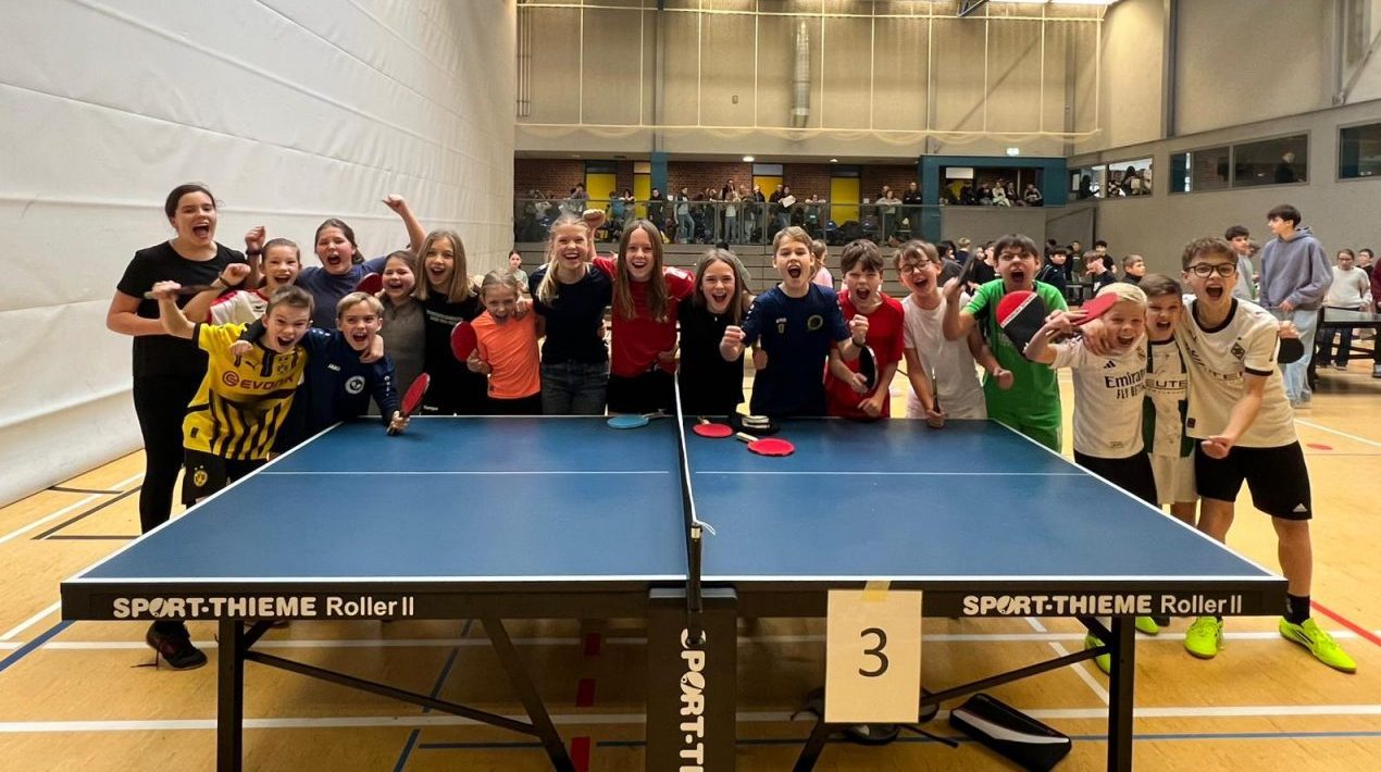 Teilnehmerinnen und Teilnehmer des Milch-Cups jubelnd um eine Tischtennisplatte positioniert